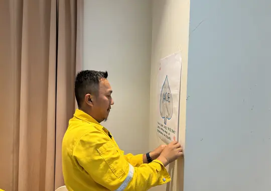 A participant in coveralls writing on the wall chart