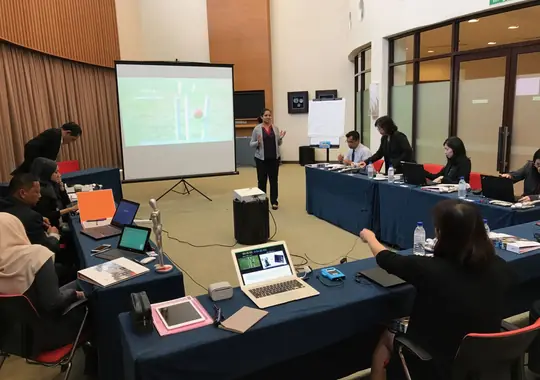 A workshop room with participants at tables and a facilitator